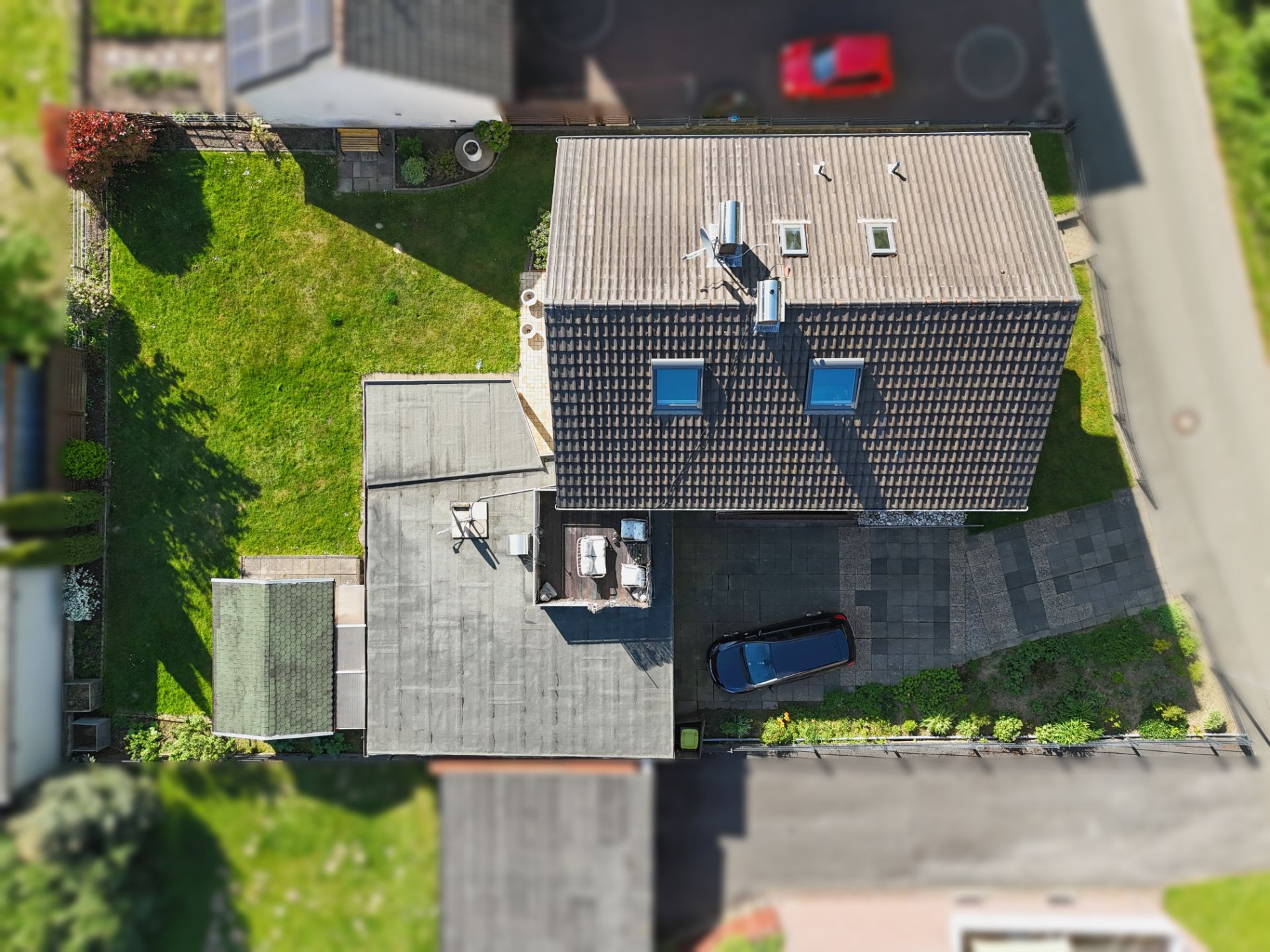 Luftaufnahme eines Wohnhauses mit Garten, Einfahrt und geparktem Auto.