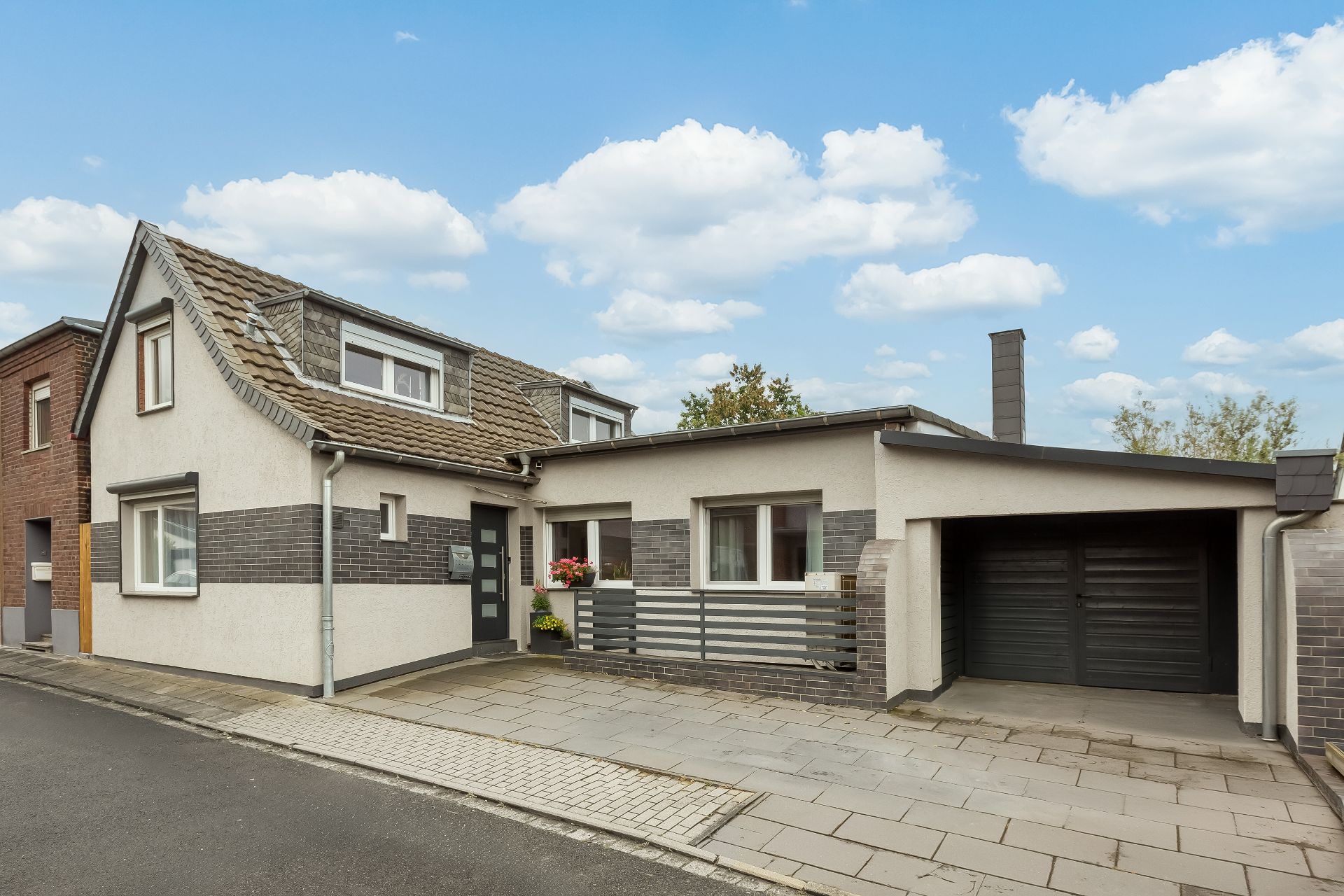 Modernes Wohnhaus mit Garage, gepflastertem Gehweg und Blumenkästen am Eingang.