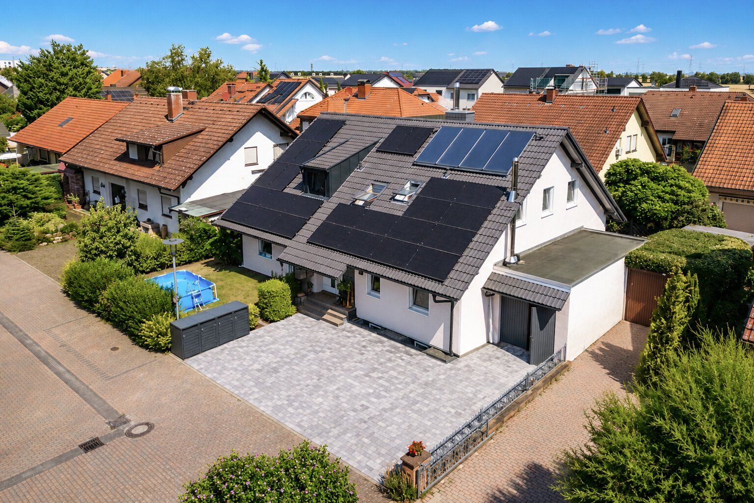 Weißes Einfamilienhaus mit Solarpanels auf dem Dach und gepflasterter Einfahrt.