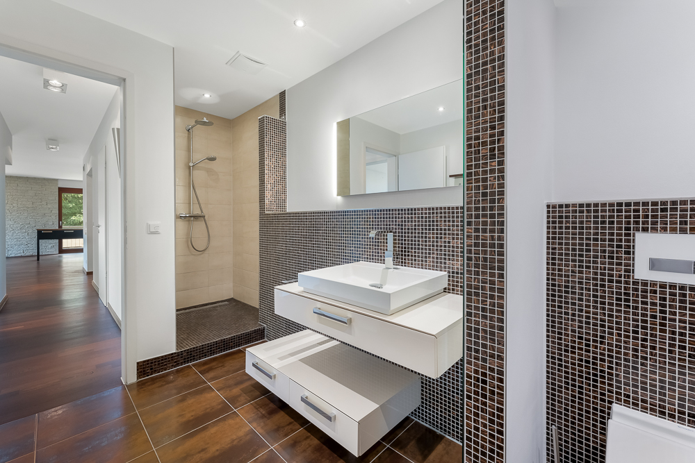 Modernes Badezimmer mit Duschbereich, Waschbecken und großem Spiegel, braune Fliesen an Wand und Boden.