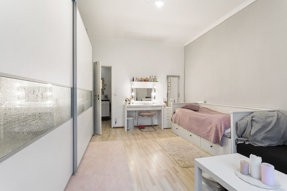 Helles Schlafzimmer mit Einzelbett, Schminktisch, großem Schrank und kleinem Tisch mit Kerzen.