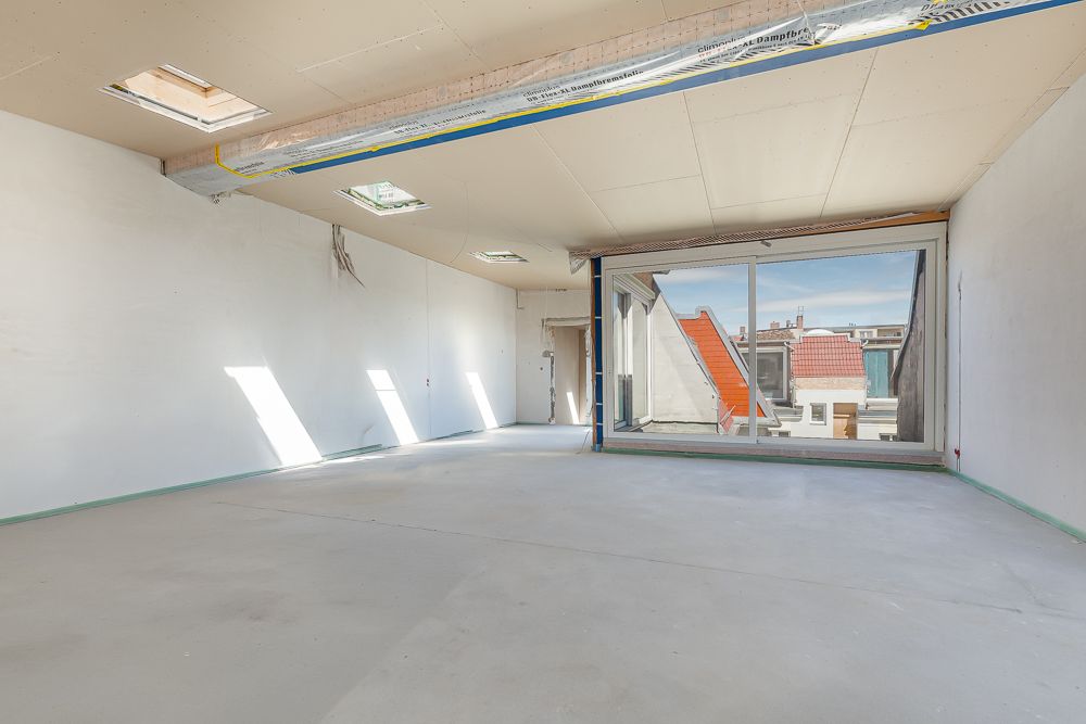 Heller, leerer Raum mit großen Fenstern und Dachfenstern in einem Wohngebäude.