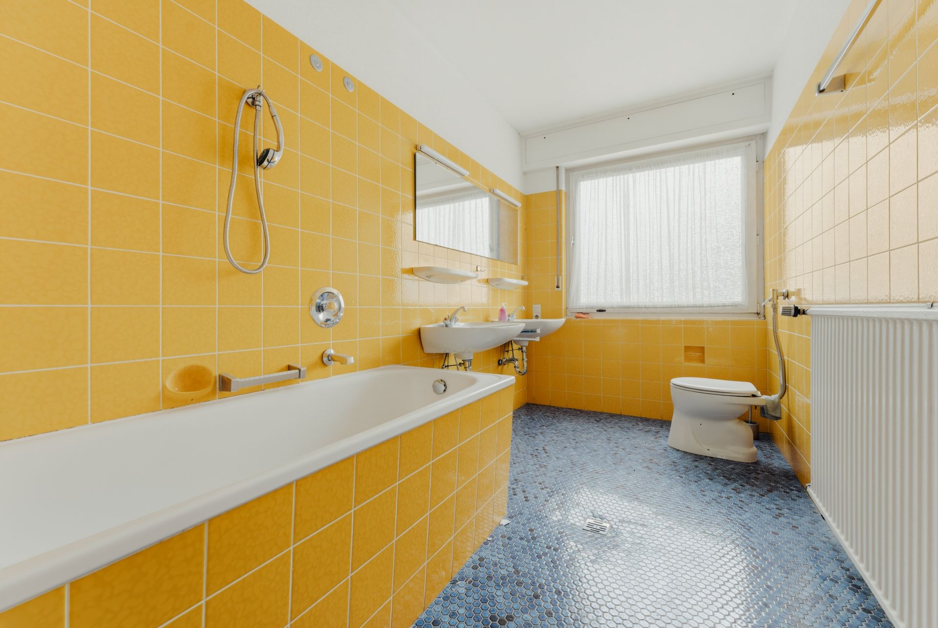 Badezimmer mit gelben Fliesen, Badewanne, Waschbecken, WC und großem Fenster.