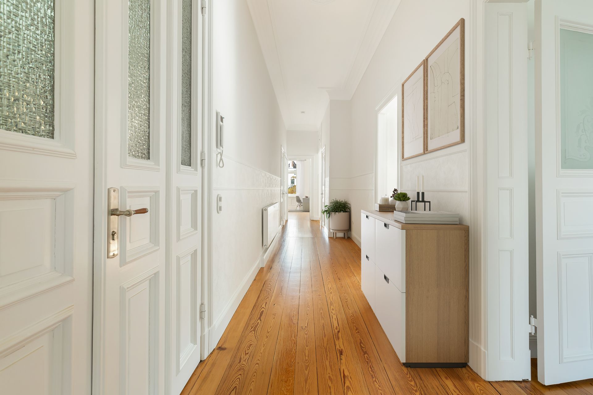 Heller Flur mit Holzboden, Kommode und Wandbildern in einer Wohnung.
