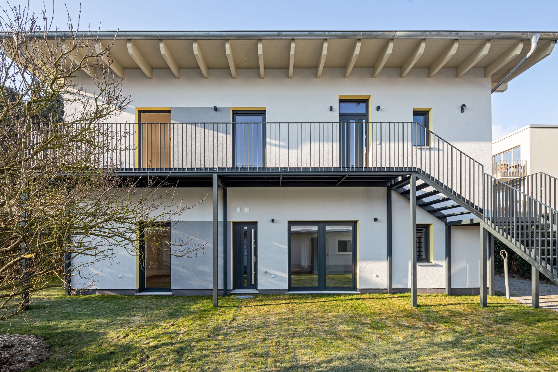 Zweistöckiges Wohnhaus mit Balkon, Außentreppe und großem Fenster im Erdgeschoss.