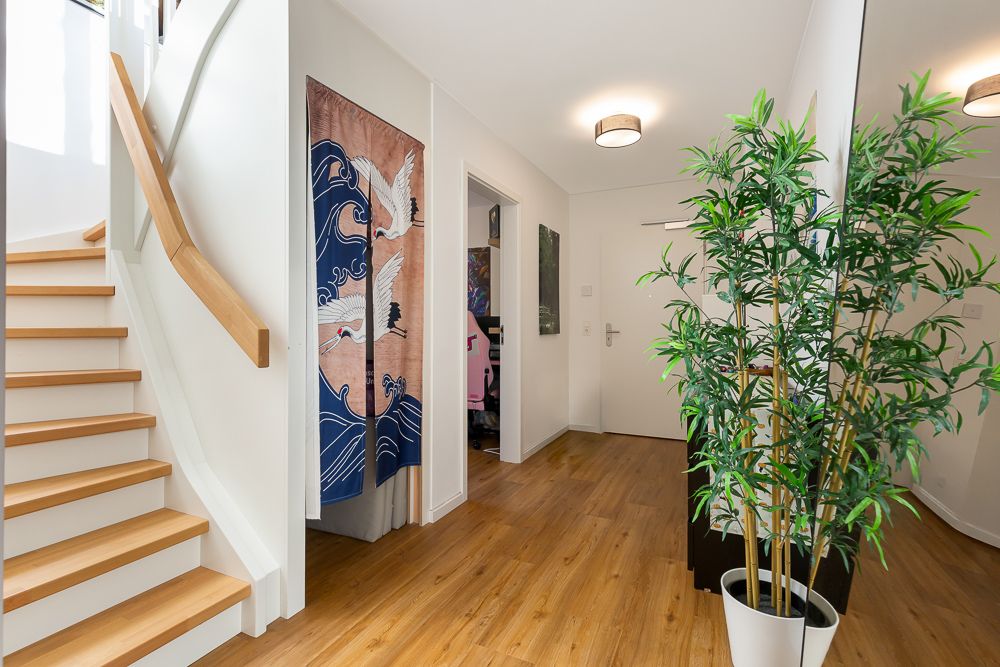 Heller Flur mit Holztreppe, Pflanze, großem Spiegel und buntem Vorhang mit Kranichmotiv.