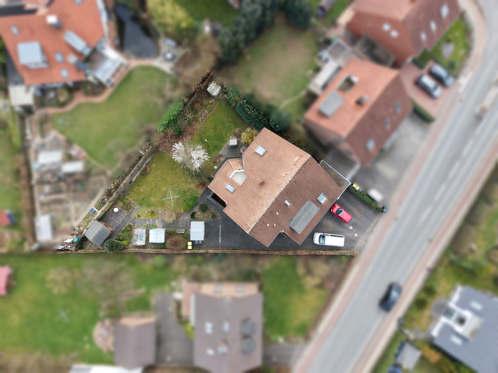 Luftaufnahme eines Hauses mit Garten, Einfahrt und geparkten Autos in einer Wohngegend.