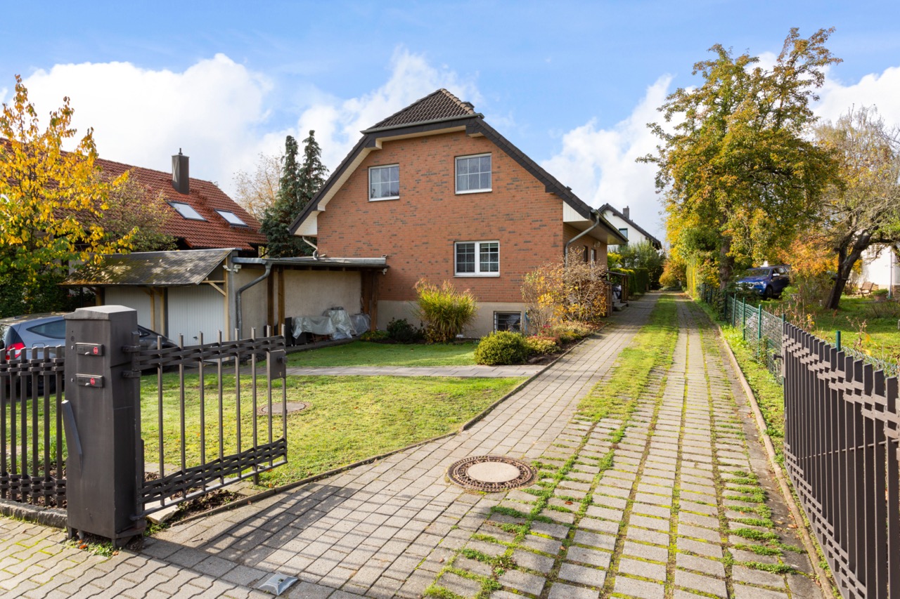 Backsteinhaus mit Satteldach, Einfahrtstor, Garten und gepflastertem Weg.