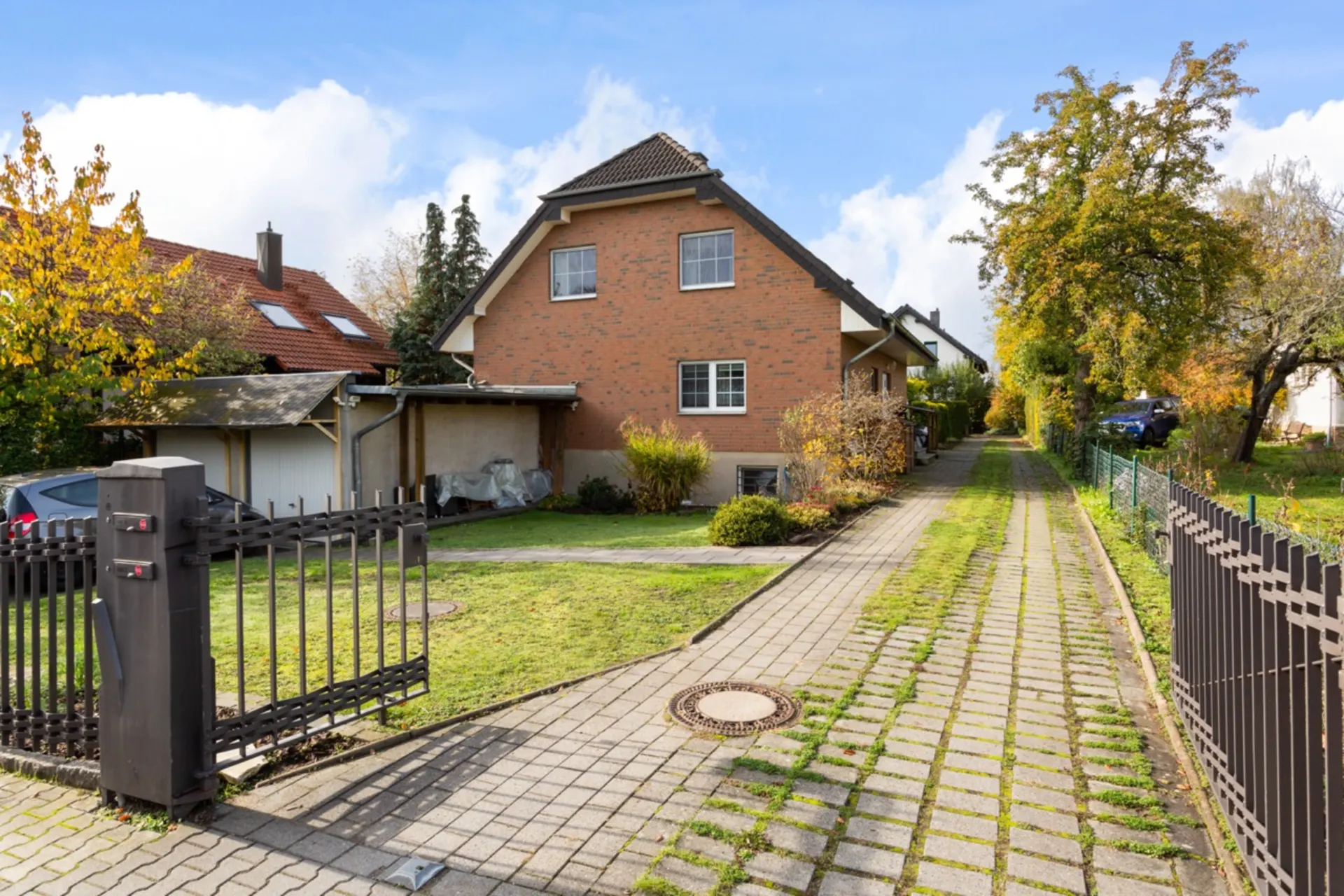 Backsteinhaus mit Satteldach, Einfahrtstor, Garten und gepflastertem Weg.