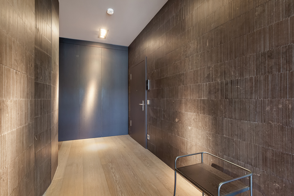 Moderner Flur mit brauner Wandverkleidung, Holzboden und kleinem Metalltisch.