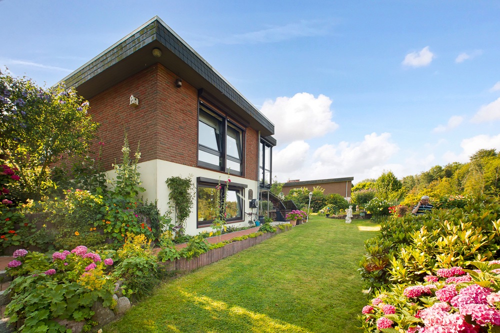 Modernes Wohnhaus mit großen Fenstern und gepflegtem Garten voller Blumen.