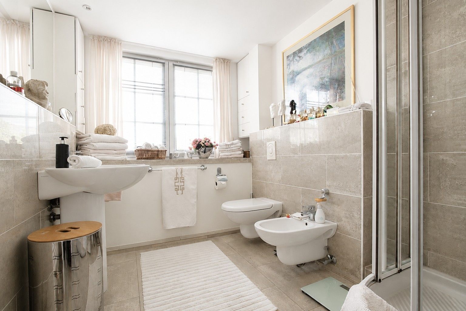 Helles Badezimmer mit Waschbecken, Toilette, Bidet, Dusche und großem Fenster.