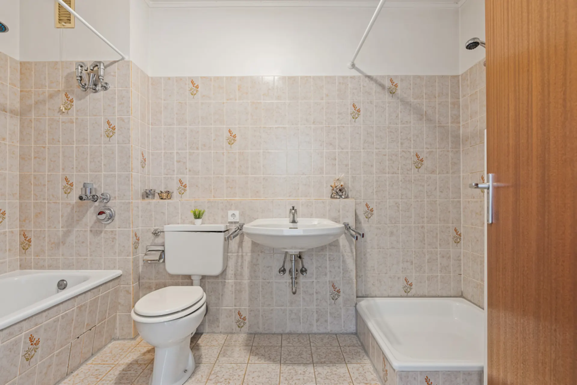 Badezimmer mit Badewanne, Toilette, Waschbecken und Dusche, gefliest mit beigen Fliesen.
