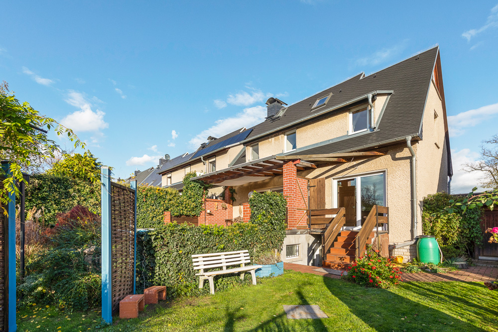 Zweistöckiges Wohnhaus mit Garten, Bank, Terrasse und Treppe im Sonnenschein.