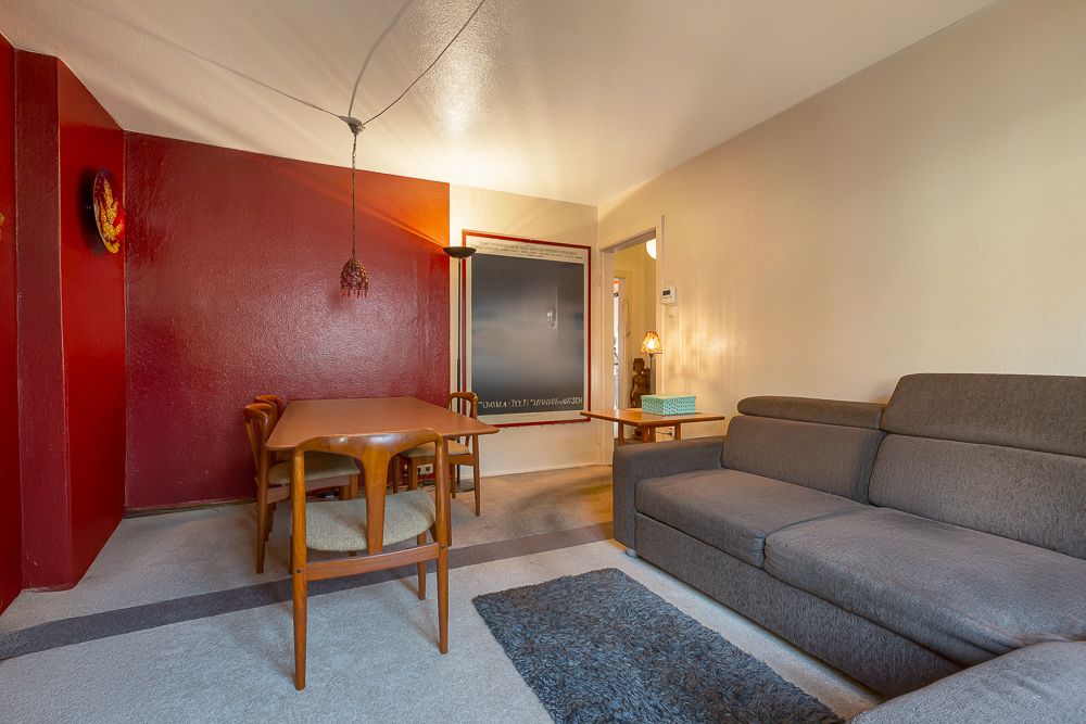 Wohnzimmer mit grauem Sofa, Holztisch und vier Stühlen vor roter Wand.