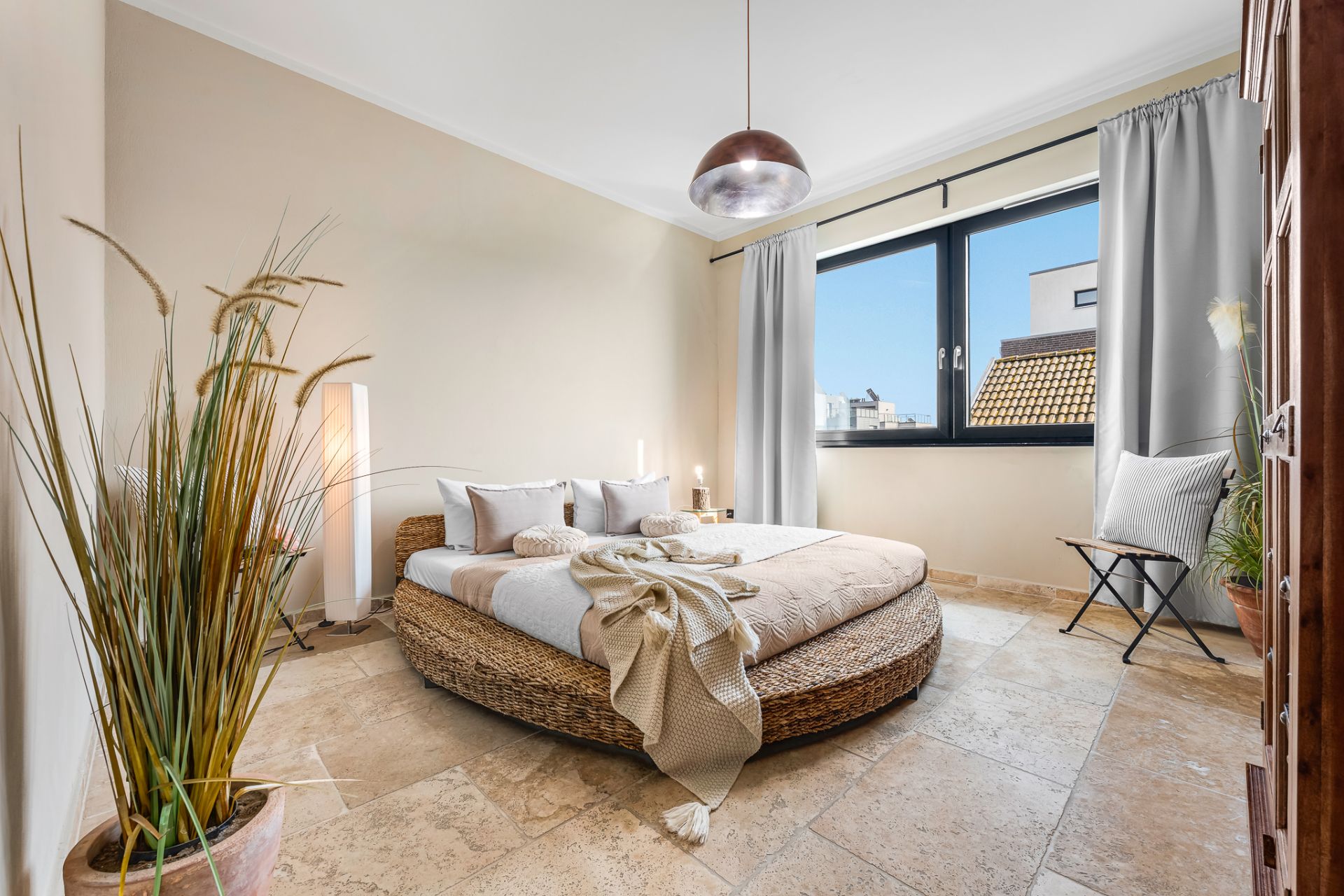 Helles Schlafzimmer mit rundem Bett, großen Fenstern, Vorhängen und Dekopflanzen.