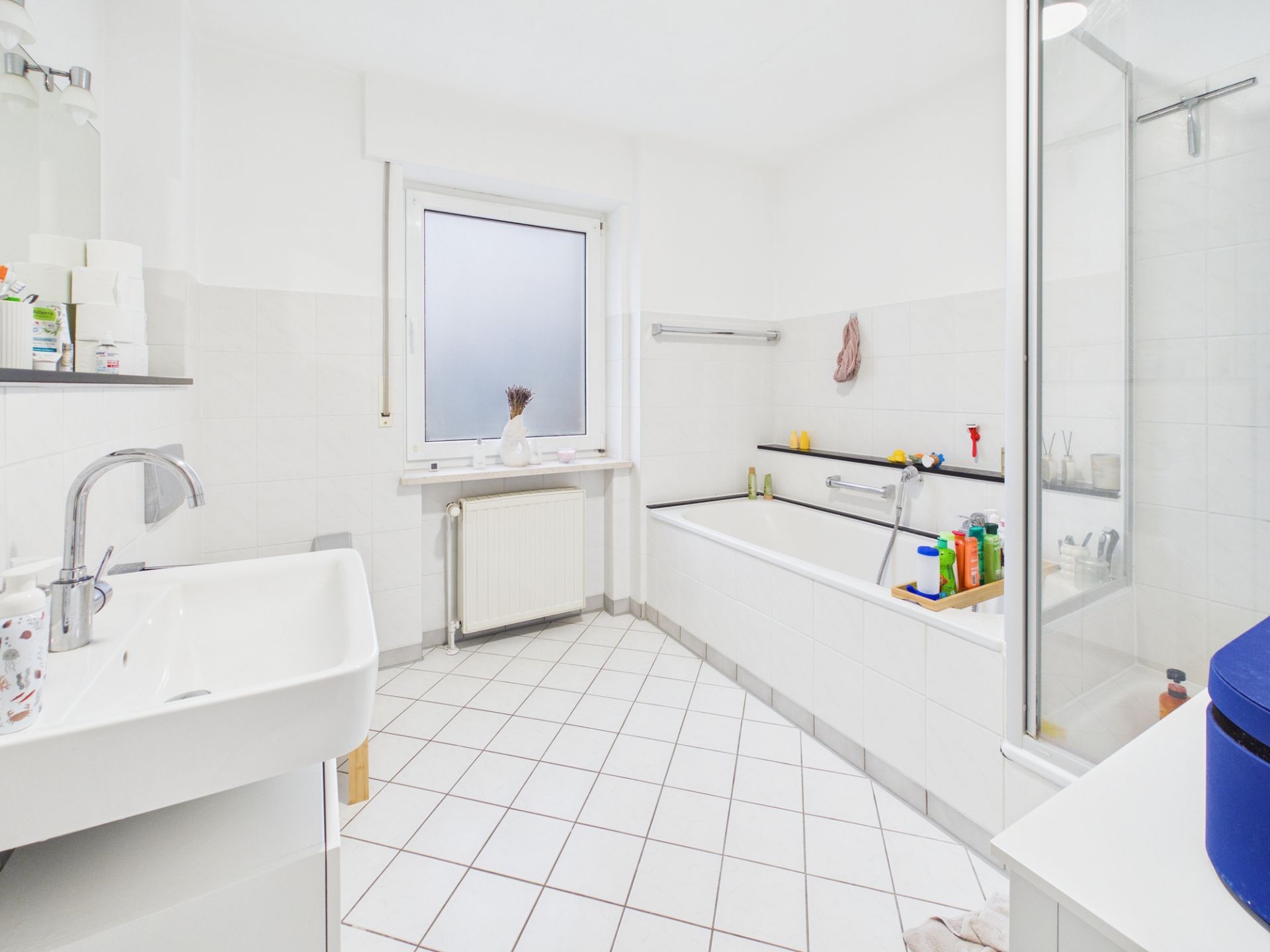 Helles Badezimmer mit Waschbecken, Badewanne, Dusche und großem Fenster.