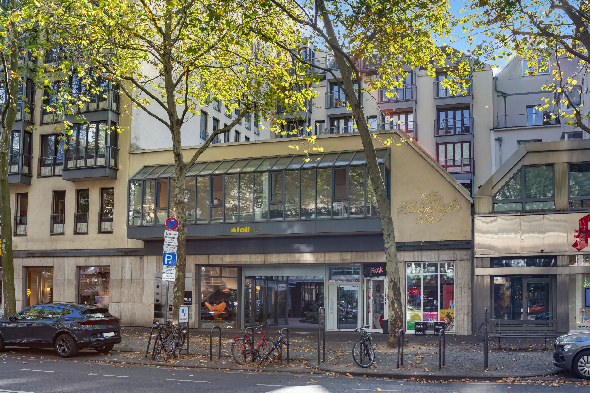 Mehrstöckiges Wohngebäude mit großen Fenstern, Bäumen und geparkten Fahrrädern vor dem Eingang.