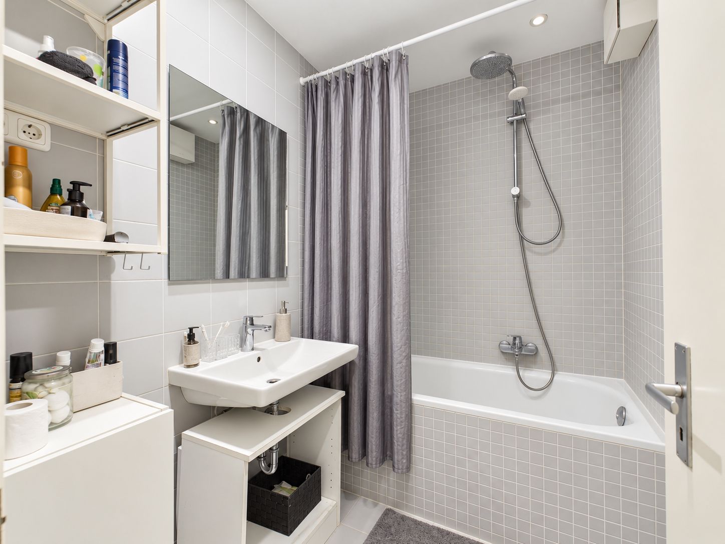 Modernes Badezimmer mit Badewanne, Waschbecken, Spiegel und grauem Duschvorhang.