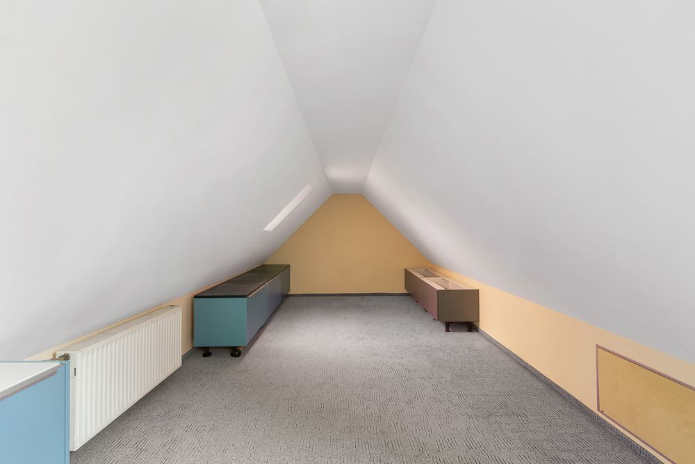 Schmaler Dachbodenraum mit Teppichboden, zwei niedrigen Schränken und gelben Wänden.