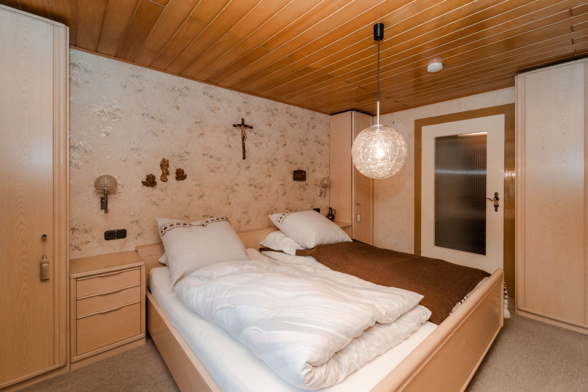 Gemütliches Schlafzimmer mit Doppelbett, Holzmöbeln und Kreuz an der Wand.
