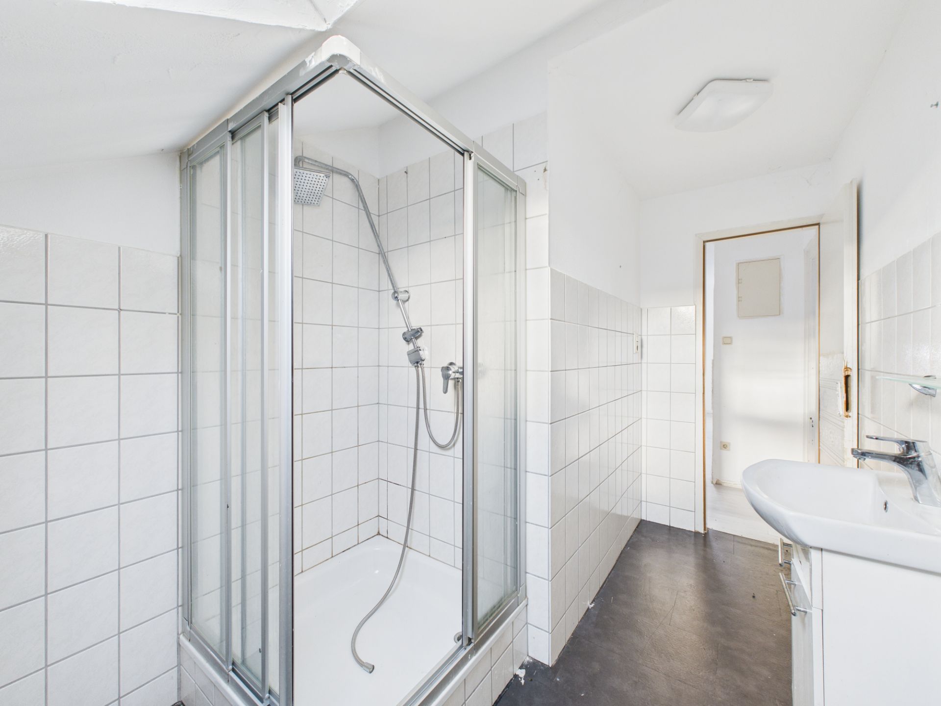 Helles Badezimmer mit Dusche, Waschbecken und weißen Fliesen an den Wänden.