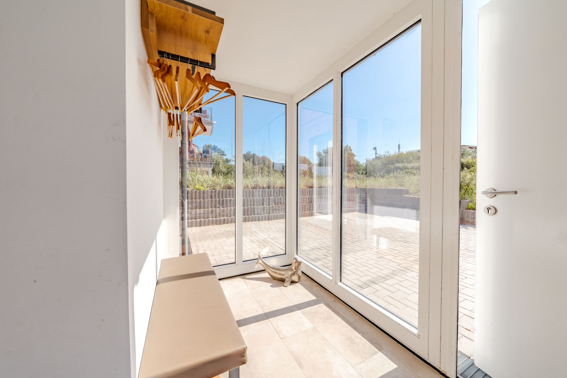Heller Flur mit großen Glasfenstern, Garderobe, Bank und Blick auf Terrasse.