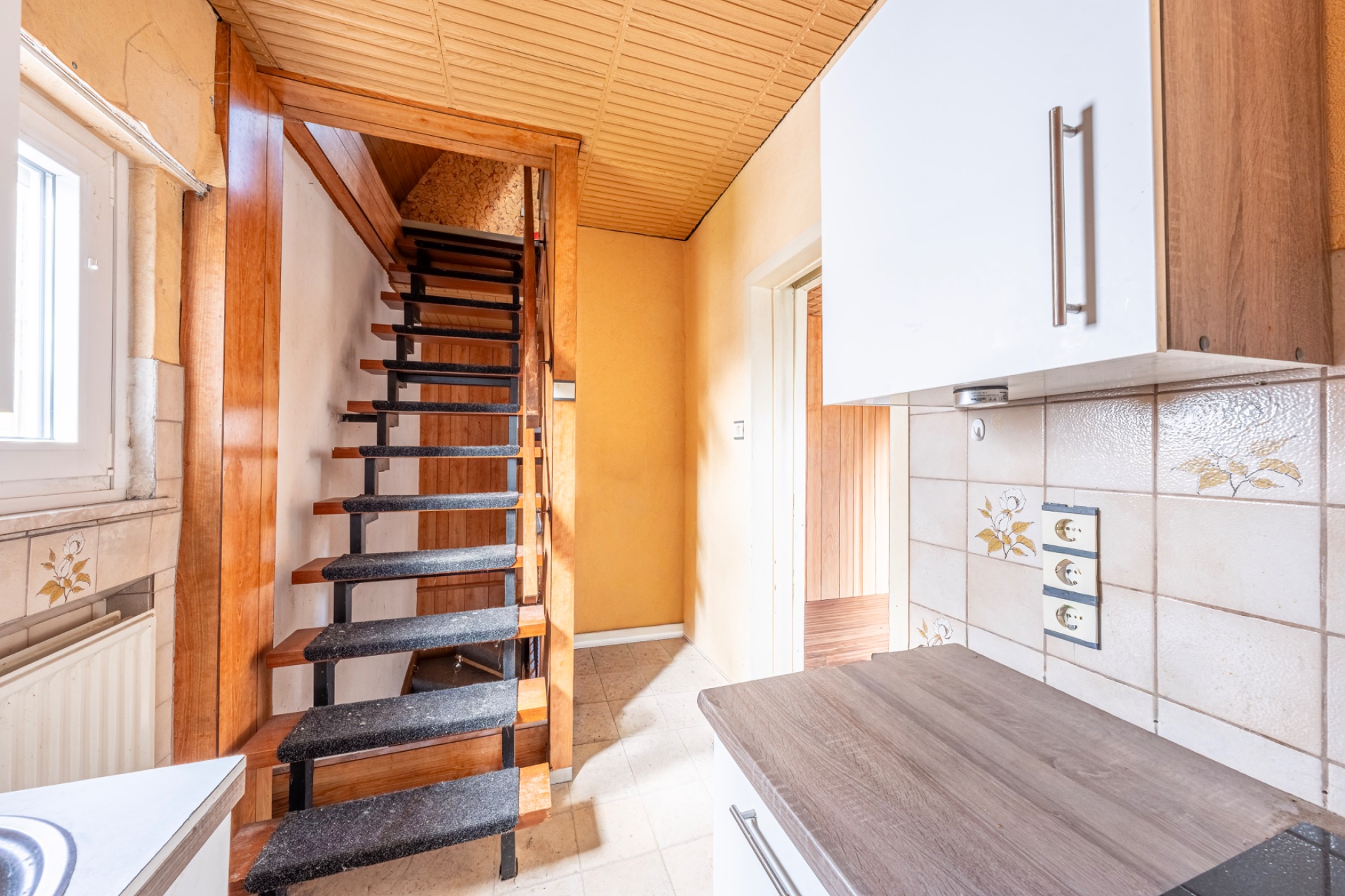 Helle Küche mit Holztreppe und Fliesenwand mit Steckdosen.