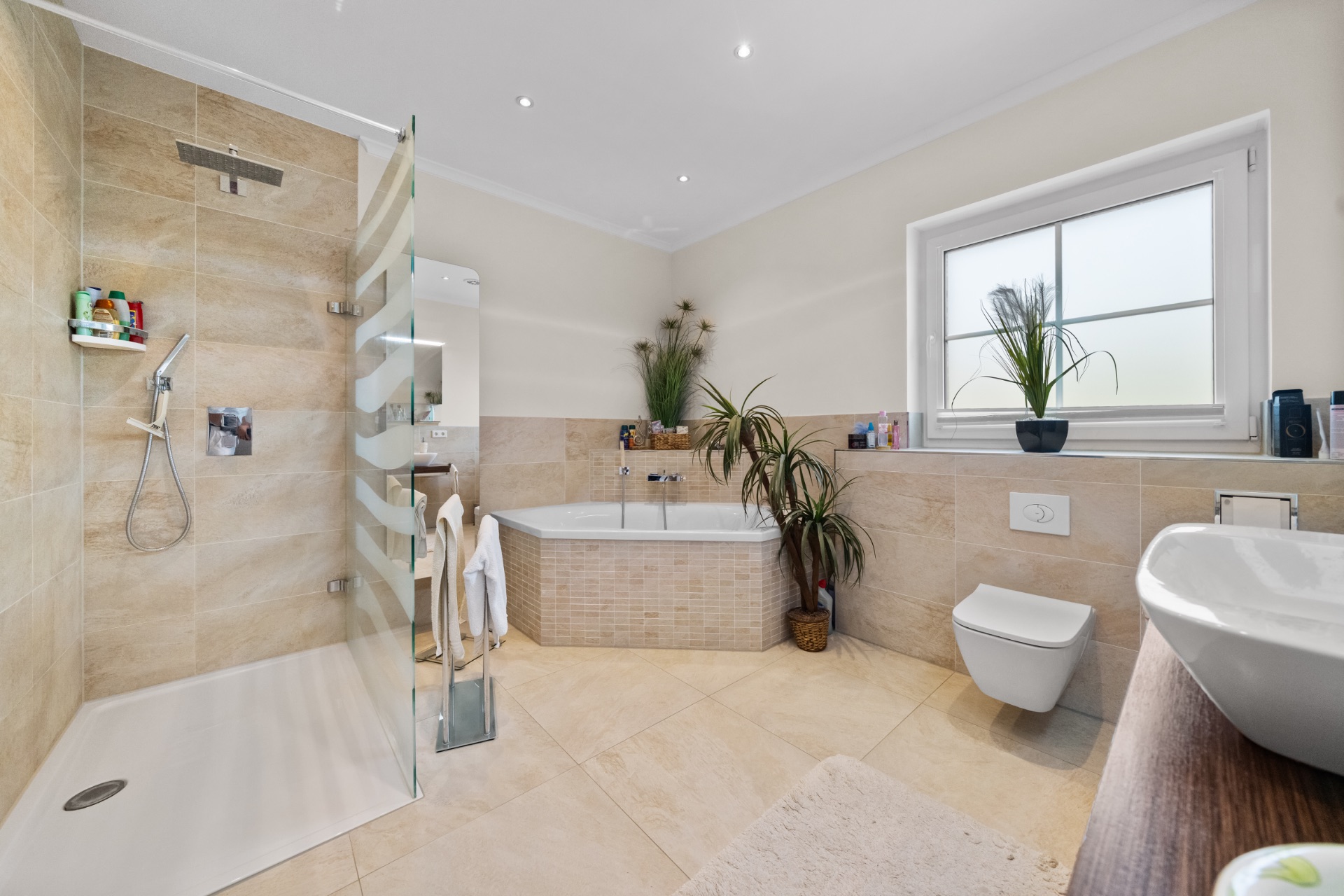 Modernes Badezimmer mit Dusche, Badewanne, WC, Pflanzen und großem Fenster.