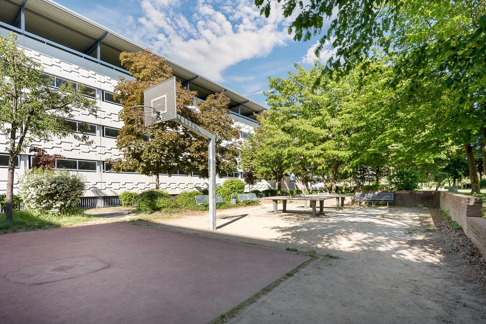 Basketballkorb und Tischtennisplatte im Innenhof eines Wohngebäudes mit Bäumen.