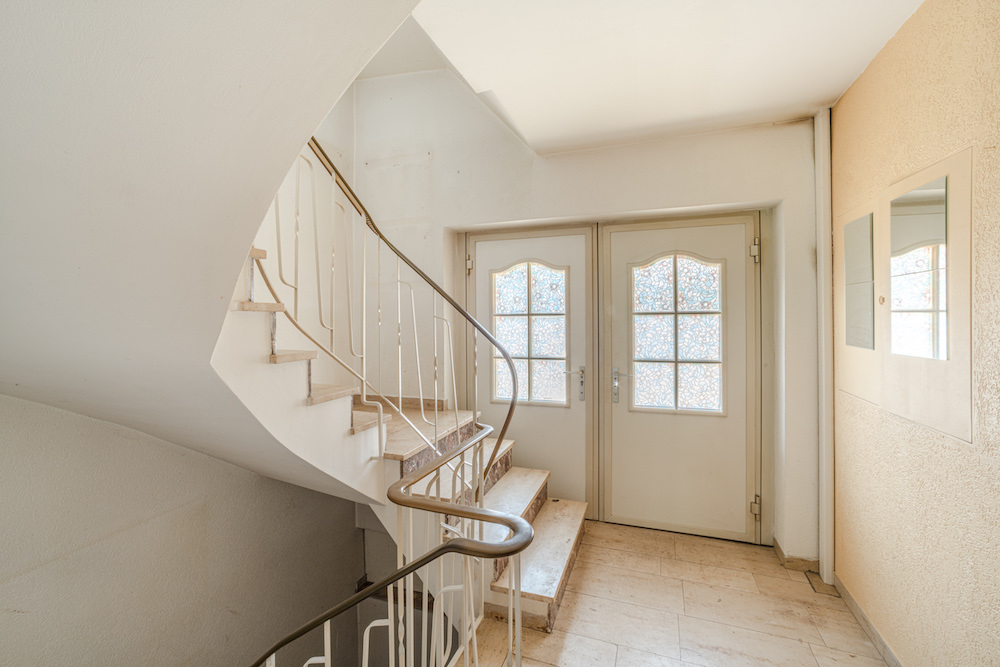 Helles Treppenhaus mit Wendeltreppe und zwei Türen mit verzierten Glasfenstern.