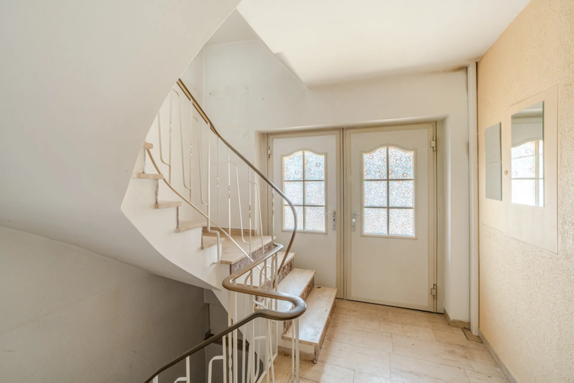 Helles Treppenhaus mit Wendeltreppe und zwei Türen mit verzierten Glasfenstern.