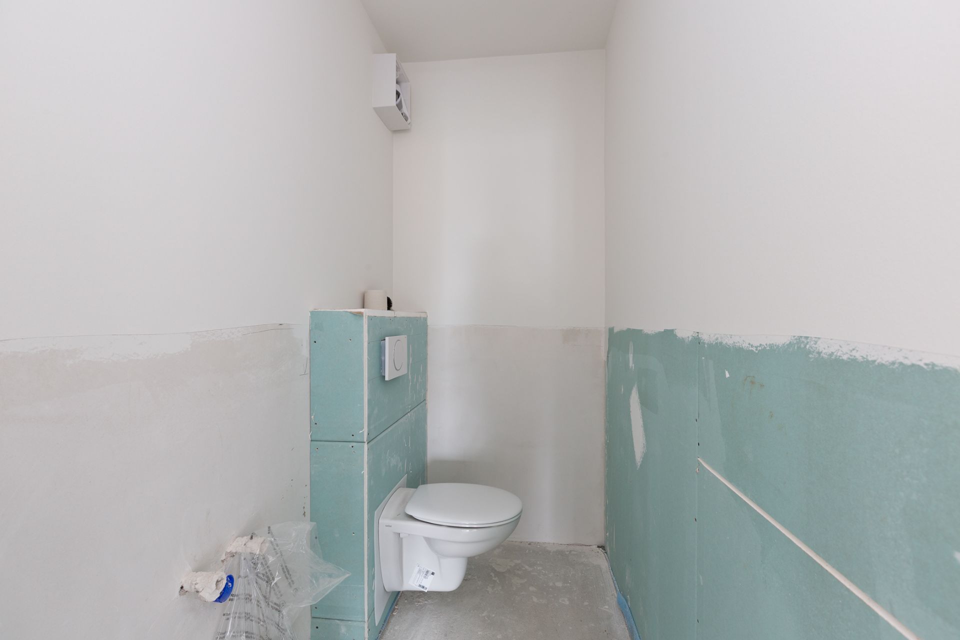 Unfertiges kleines Bad mit Wandtoilette und teilweise verputzten Wänden.