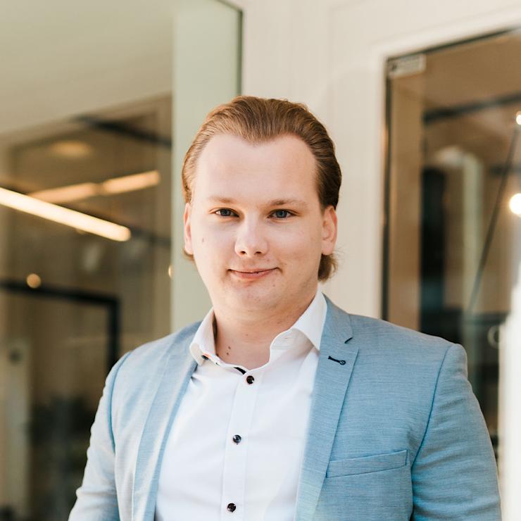 Ein junger Mann im Anzug steht in einem modernen Bürobereich.