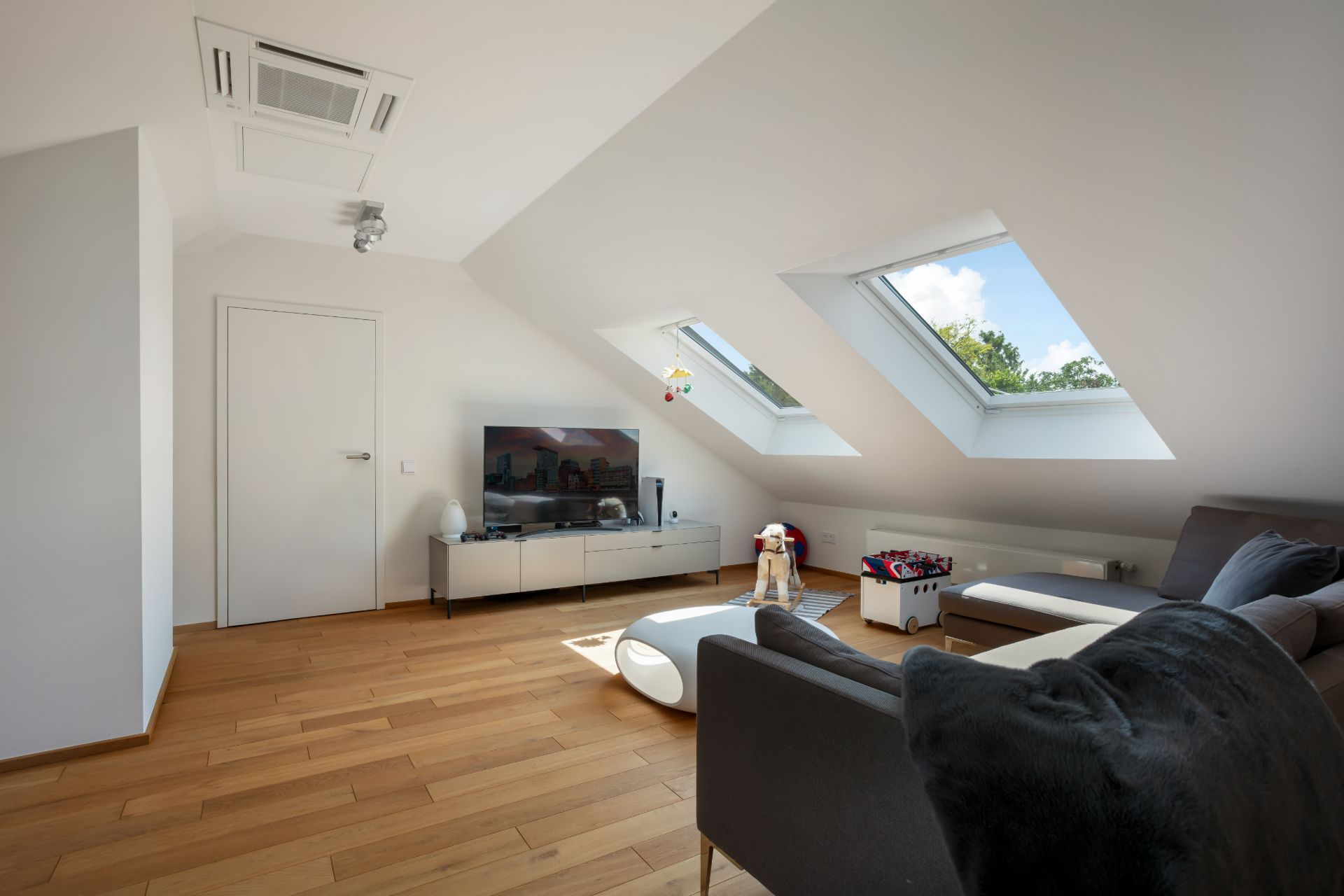 Helles Wohnzimmer mit Dachschräge, Sofa, Fernseher und zwei Dachfenstern.