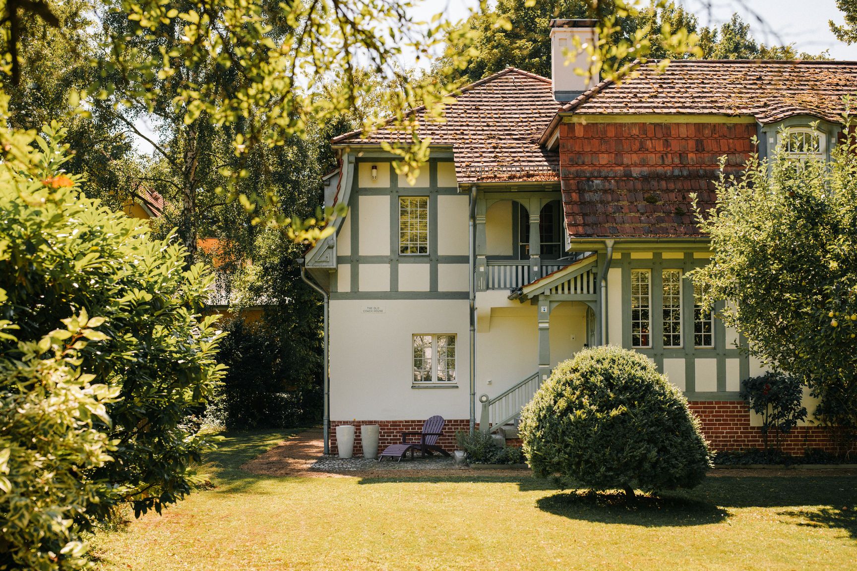 Wohnhaus mit Fachwerkelementen, Vorgarten mit Rasen und Büschen, sonniger Tag.