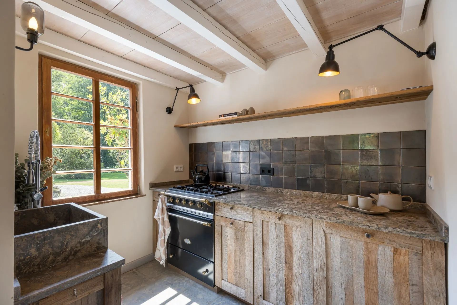 Kleine Küche mit Holzmöbeln, Gasherd, Spüle vor Fenster und offenem Regal über der Arbeitsfläche.