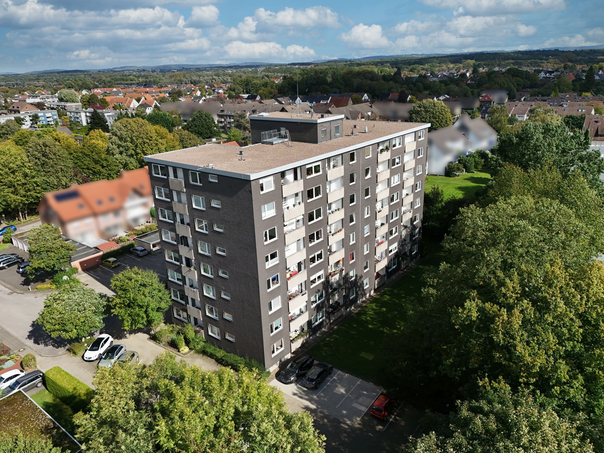 Mehrstöckiges Wohngebäude mit Flachdach, umgeben von Bäumen und parkenden Autos.
