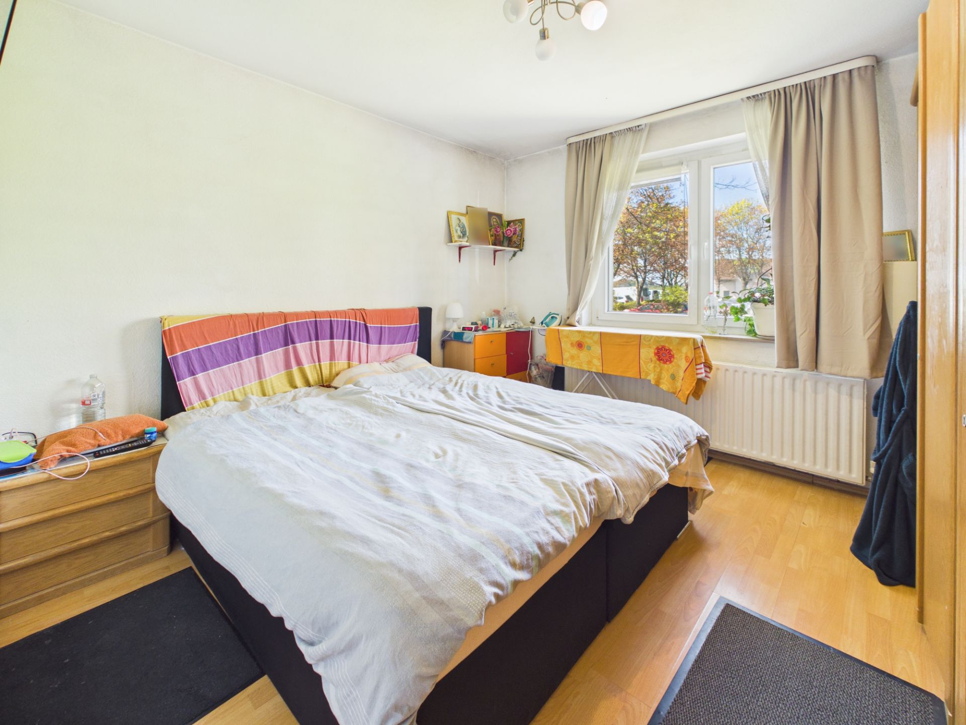 Helles Schlafzimmer mit Doppelbett, Nachttisch, Fenster mit Vorhängen und Holzboden.