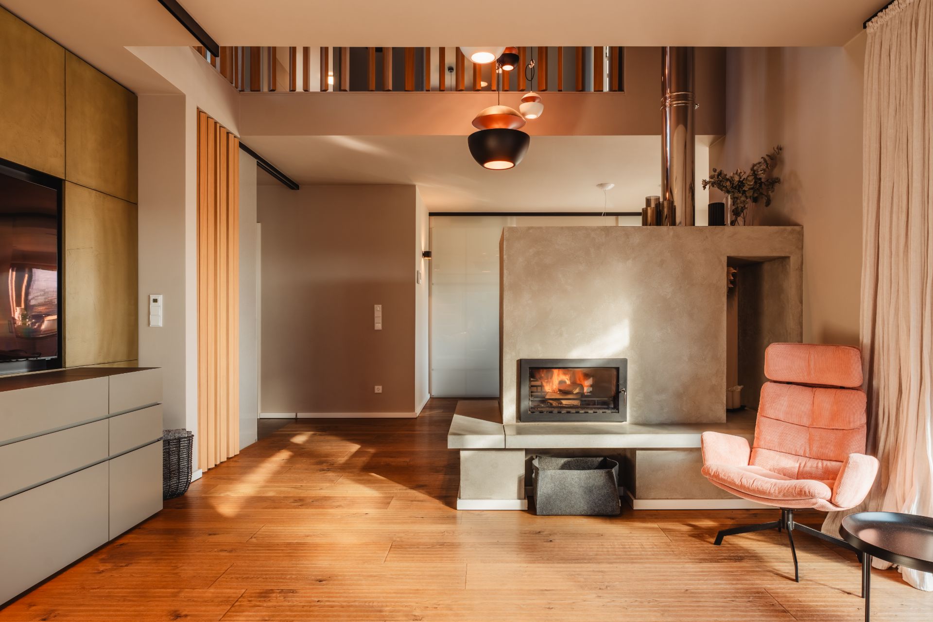 Modernes Wohnzimmer mit Holzfußboden, Kamin, rosa Sessel und großen Fenstern mit Vorhängen.