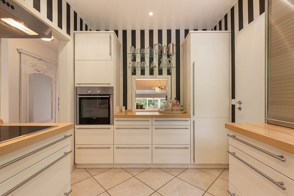 Moderne Küche mit weißen Schränken, Holzarbeitsplatten und gestreifter Wand.