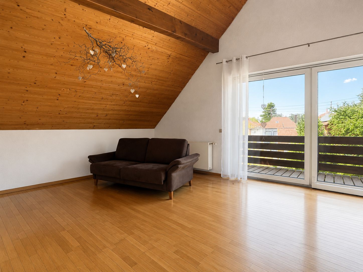 Helles Wohnzimmer mit Holzdecke, braunem Sofa und großem Fenster zum Balkon.