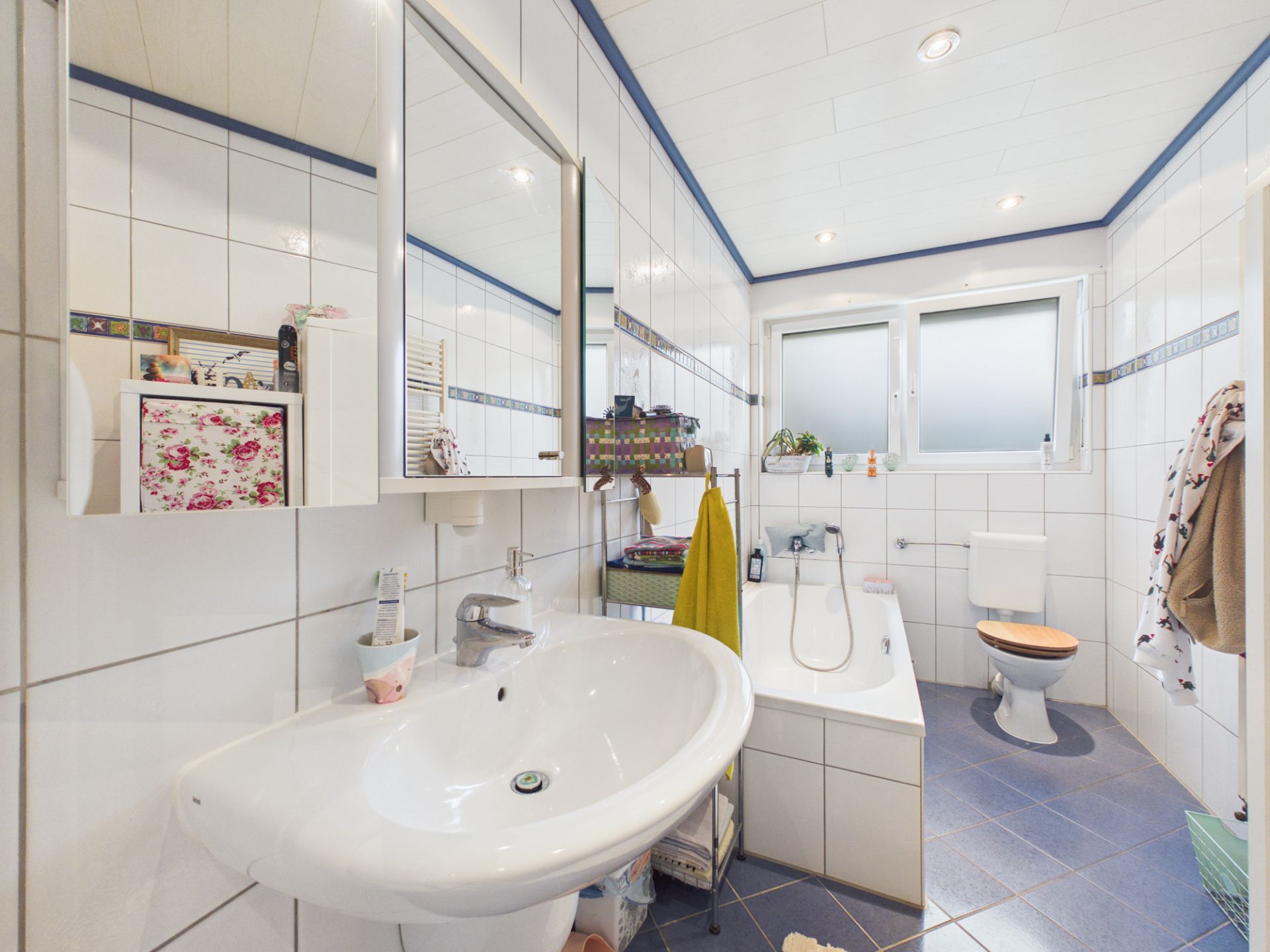 Modernes Badezimmer mit weiß gefliesten Wänden, Badewanne, Waschbecken und Fenster.