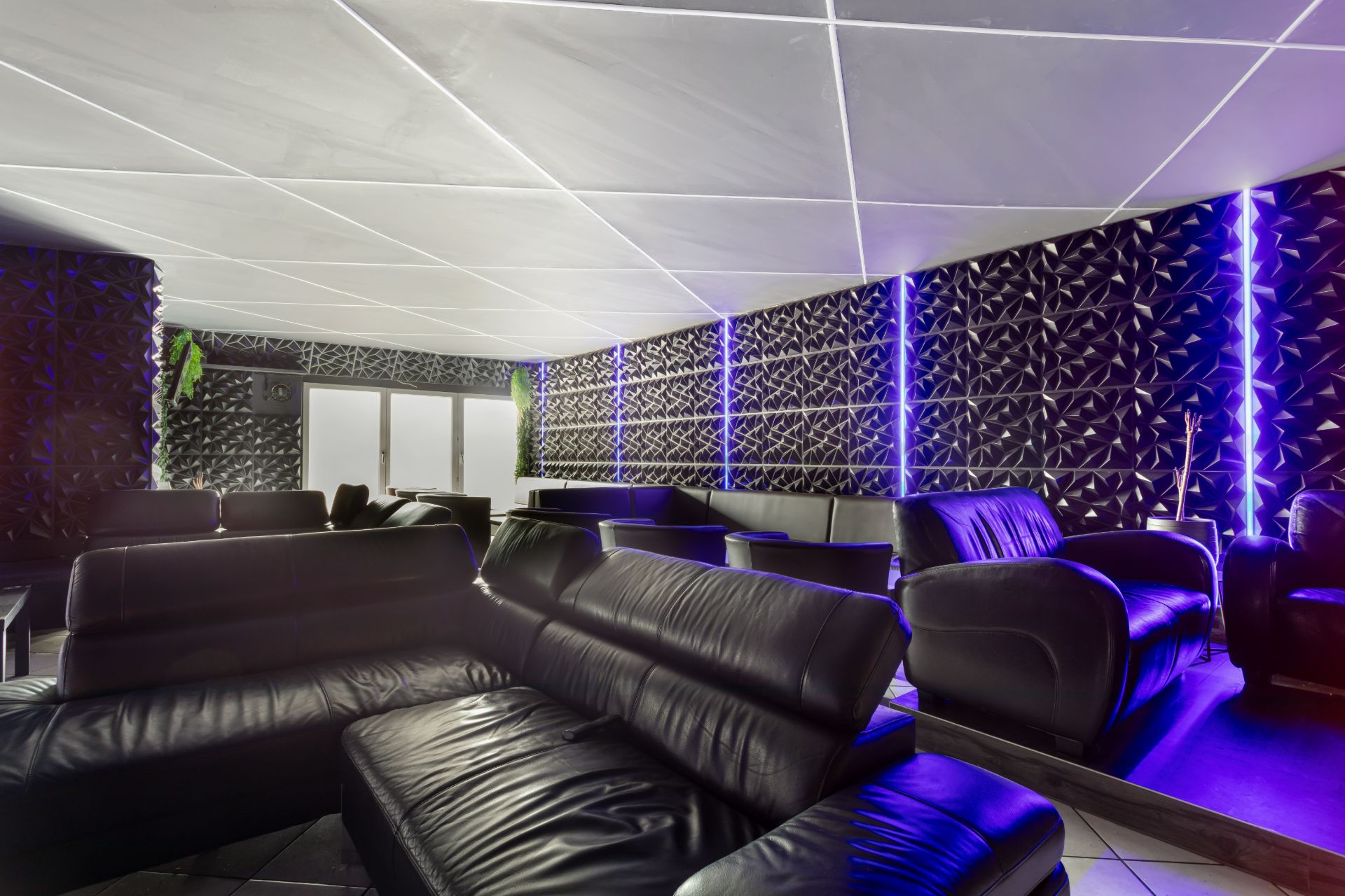 Wohnzimmer mit schwarzen Ledersofas und gemusterten Wänden mit blauer Beleuchtung.