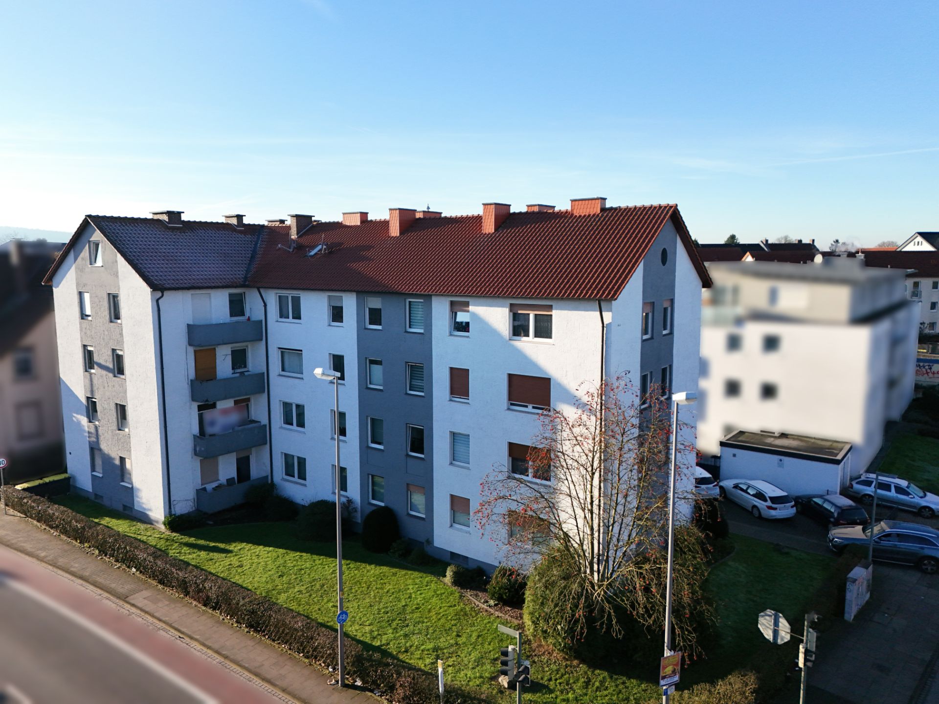 Mehrfamilienhaus mit rotem Dach, mehreren Balkonen und grüner Rasenfläche im Vordergrund.