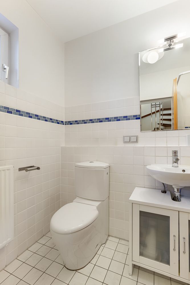 Modernes Badezimmer mit weißer Toilette, Waschbecken, Spiegel und Fliesen mit blauer Bordüre.