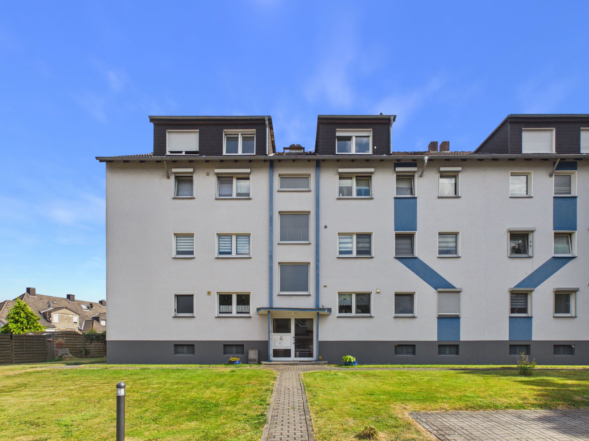 Vorderansicht eines mehrstöckigen Wohnhauses mit Eingangsbereich und Rasenfläche davor.