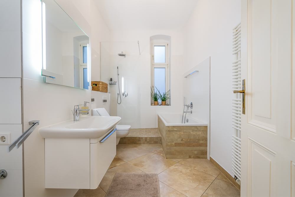Modernes Badezimmer mit Dusche, Badewanne, Waschbecken und zwei Fenstern, Pflanzen auf dem Fenstersims.