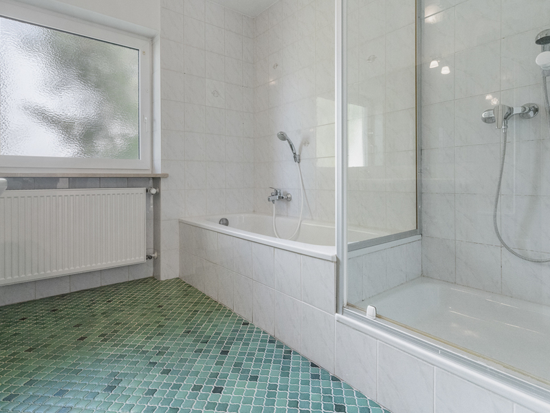 Helles Bad mit Badewanne, Dusche, grünem Fliesenboden und großem Fenster.