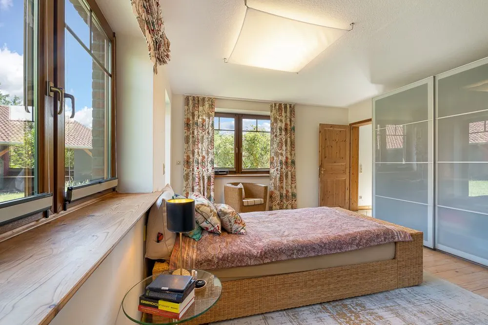 Helles Schlafzimmer mit großem Bett, Nachttisch, Fenstern und Kleiderschrank mit Schiebetüren.